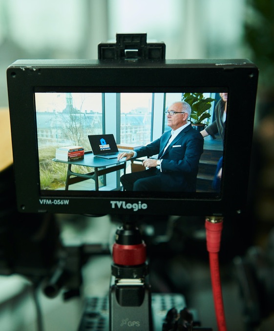 TV monitor filming Joe Navarro sitting at table in front of a window